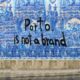 Capela das Almas, Porto, Portugal. Mural azul com desenhos detalhados de azulejos portugueses e a frase "Porto. is not a brand" escrita em preto no centro. No canto inferior direito, uma pessoa caminhando na calçada.