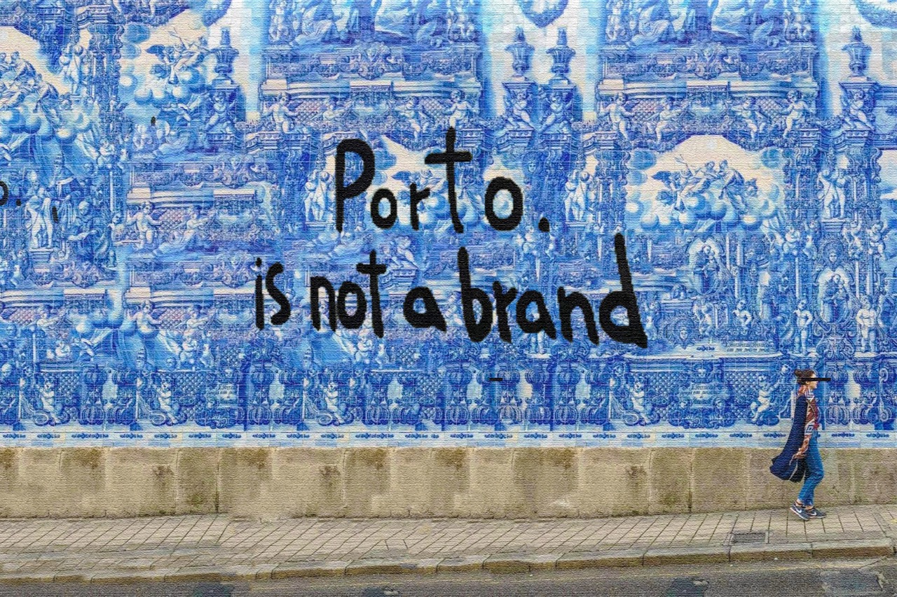 Capela das Almas, Porto, Portugal. Mural azul com desenhos detalhados de azulejos portugueses e a frase "Porto. is not a brand" escrita em preto no centro. No canto inferior direito, uma pessoa caminhando na calçada.